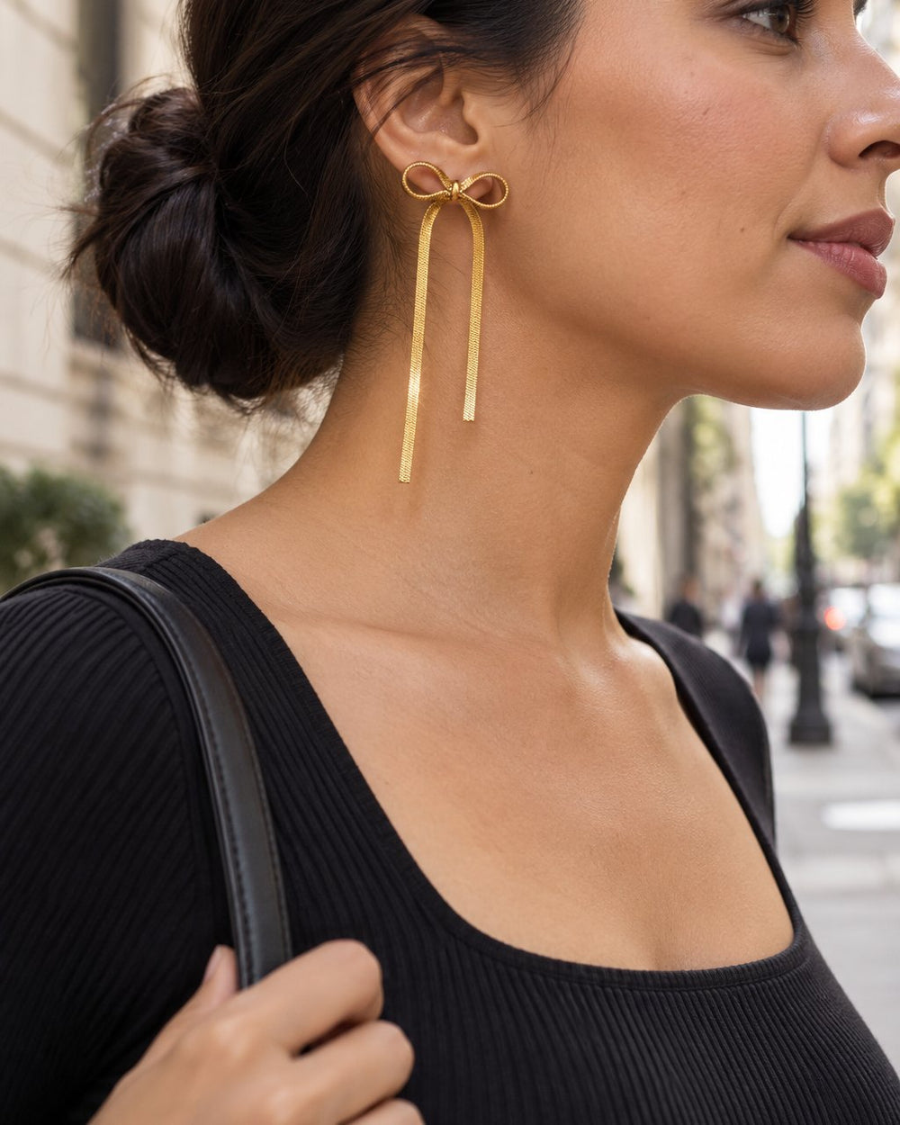 Woman with a sleek low bun wearing a gold-tone chain bow earring, its tails falling past her lobe