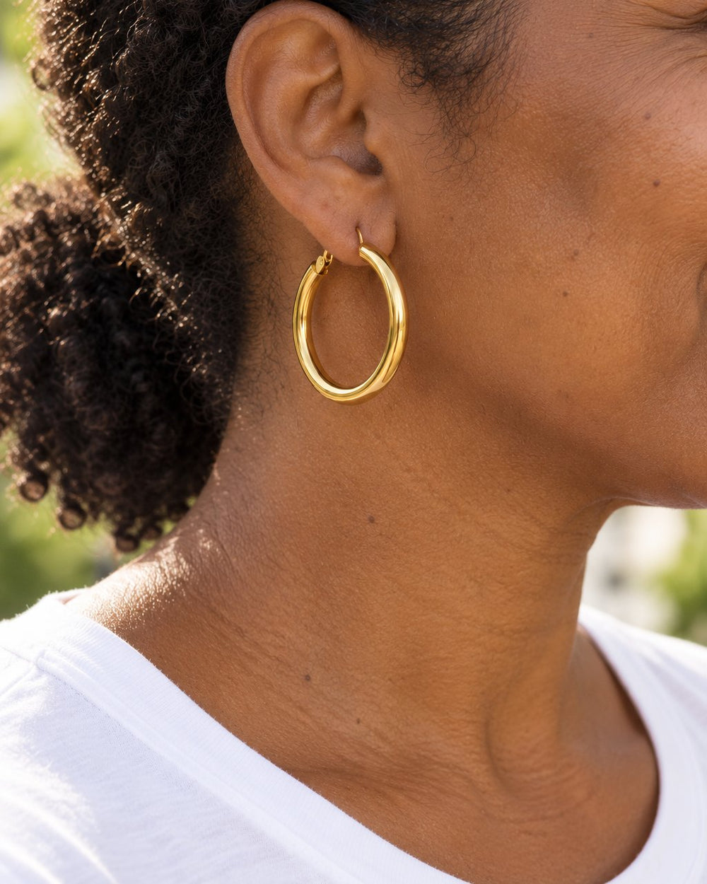 Woman with her hair in a low ponytail wearing a glossy gold-tone 1.5 in hoop