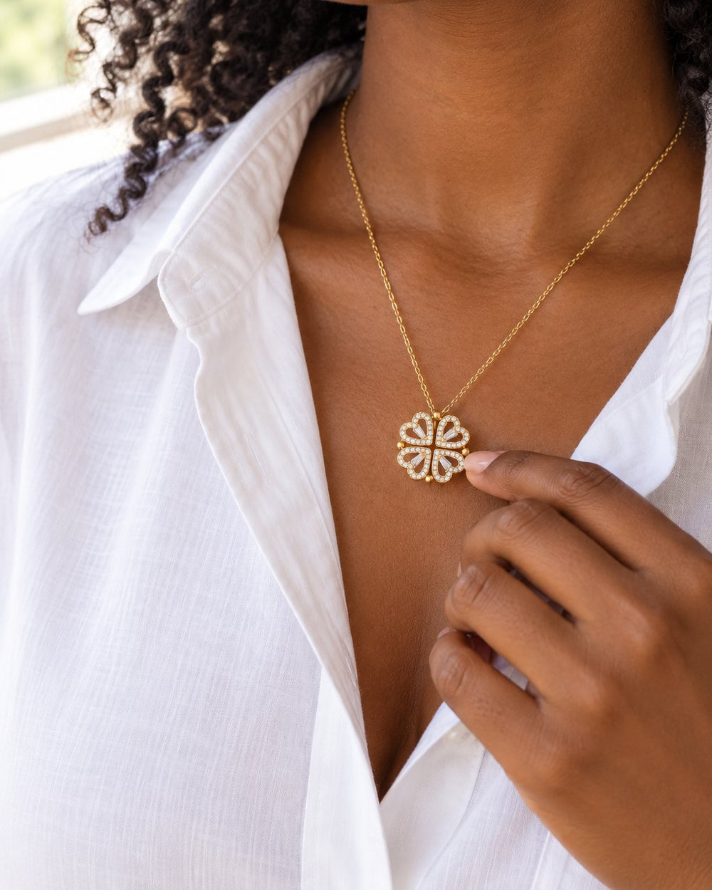 Woman in a white shirt wearing the gold-tone heart clover pendant at her collarbone, face partly cropped