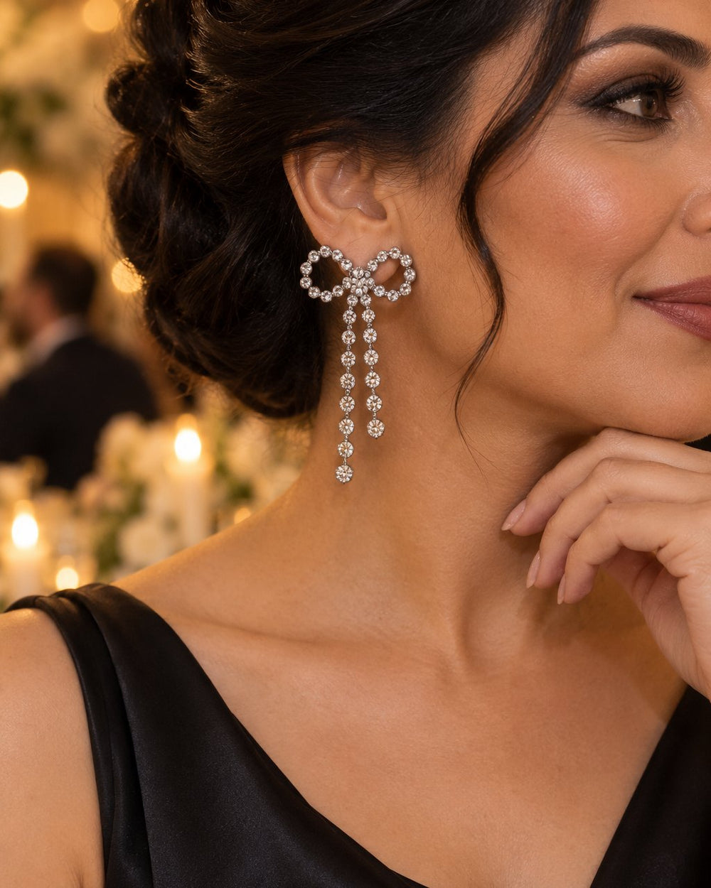 Woman with her hair swept up wearing a sparkling bow earring with long tails at an evening party