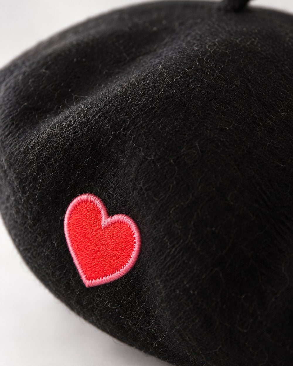 Close-up of the embroidered red heart on the soft black beret fabric