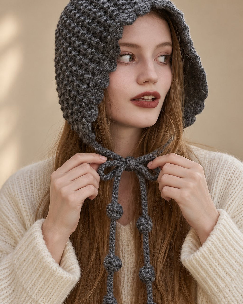 A woman ties the grey knit bonnet's long ties into a bow under her chin