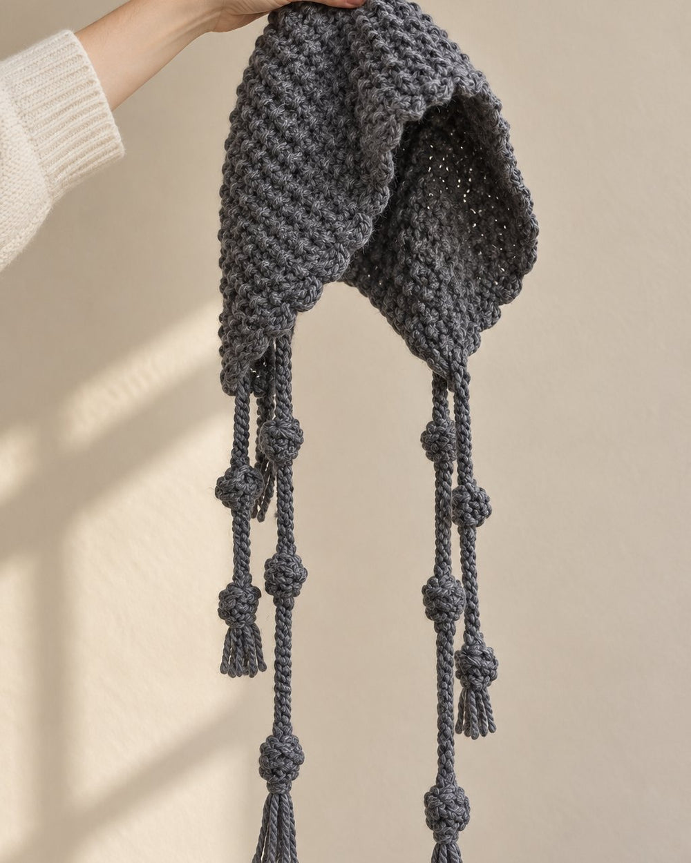 The grey knit bonnet held up by its crown, the long knotted ties hanging down