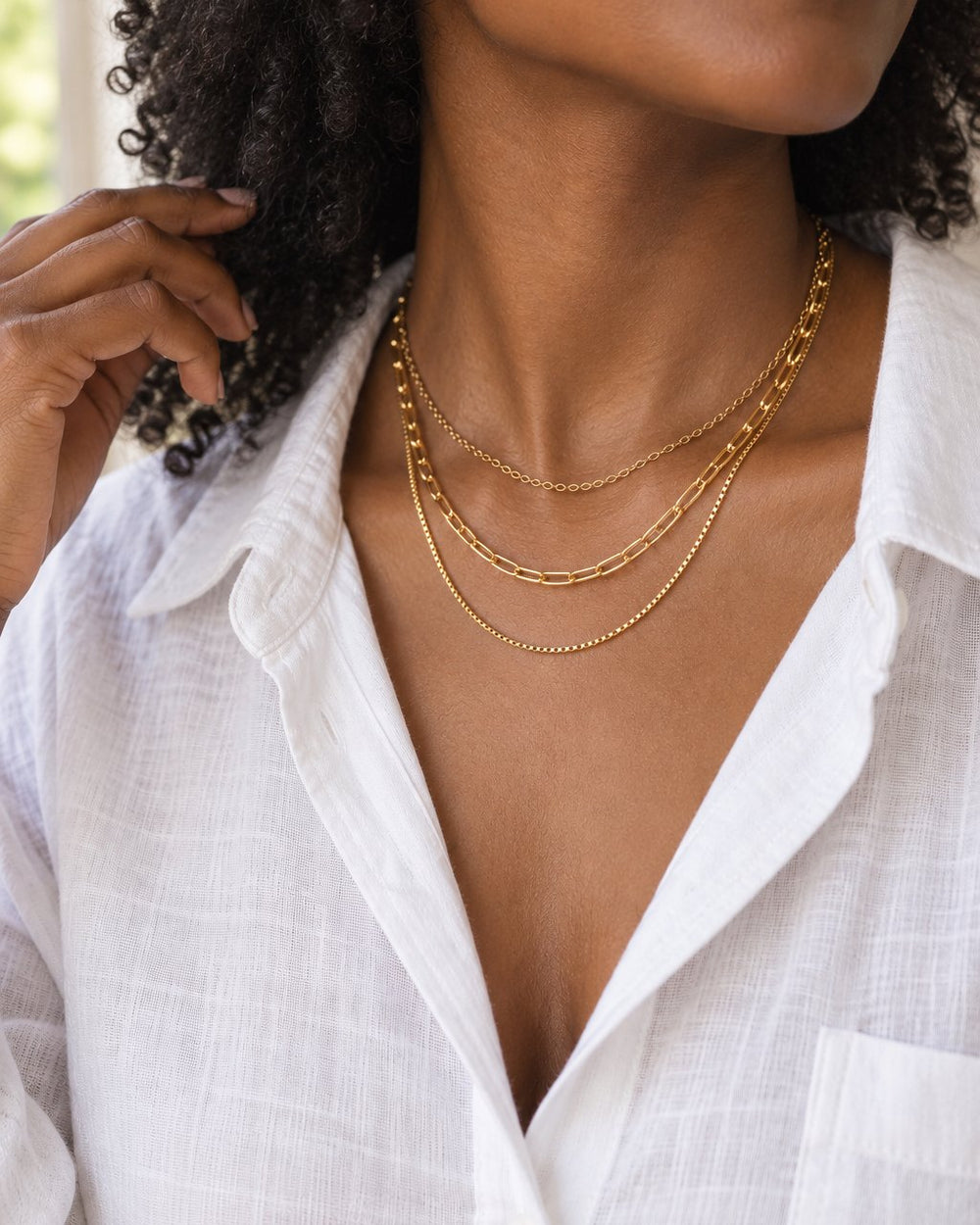 Woman in an open-collar white shirt wearing the three-layer necklace, face cropped