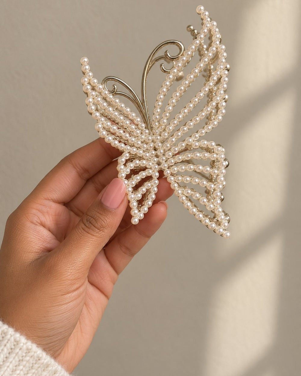 A hand holds the pearl butterfly claw clip, the wings wider than the palm