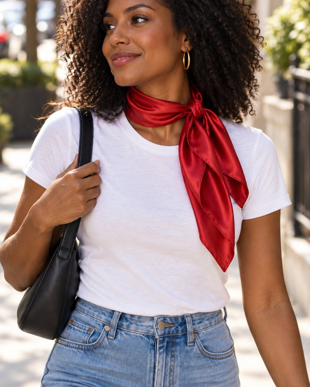 Woman on a city street with the red satin scarf knotted at her neck over a white tee