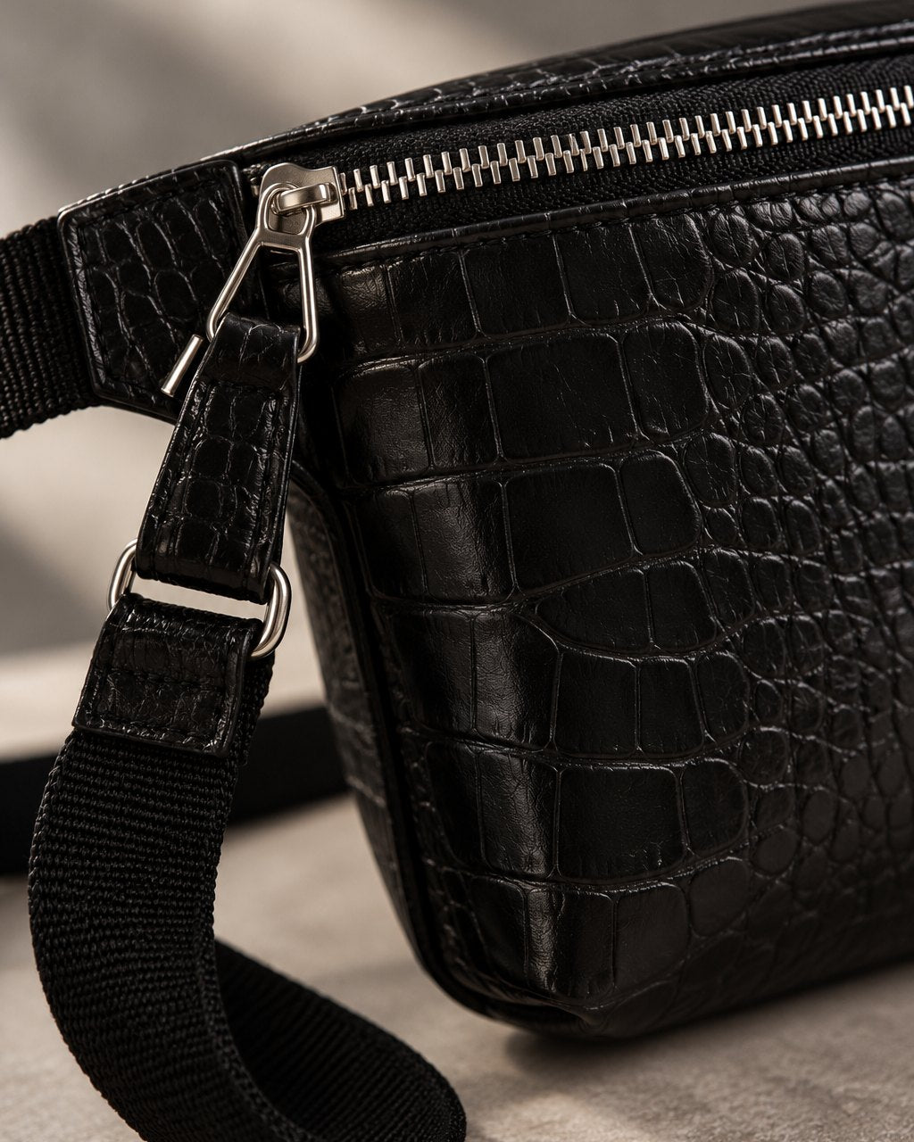 Close-up of the croc-embossed texture, the top zip and the strap's metal ring