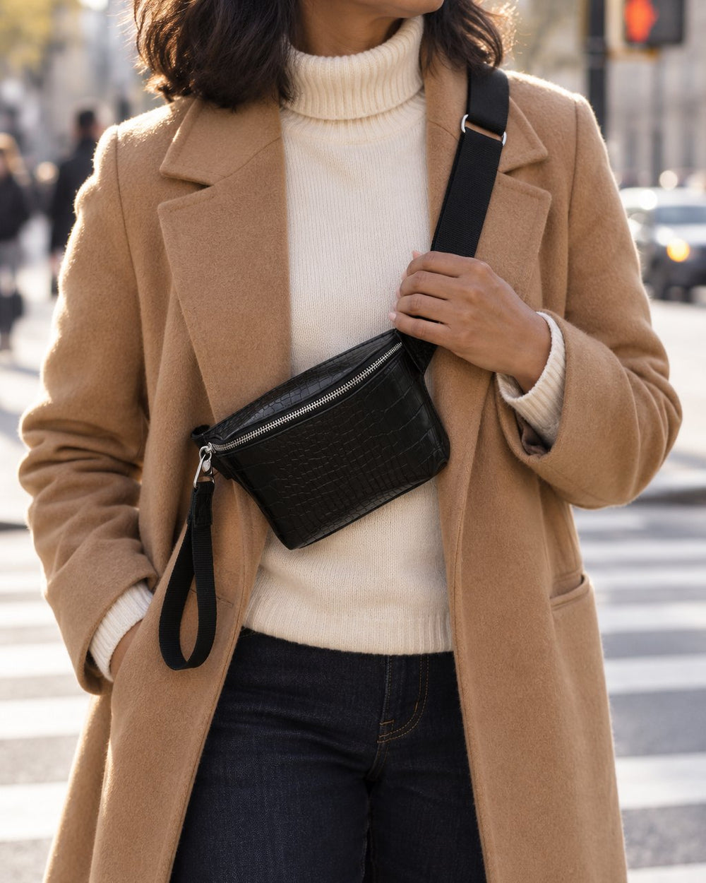 Woman in a camel coat wearing the black belt bag across her chest at a city crossing