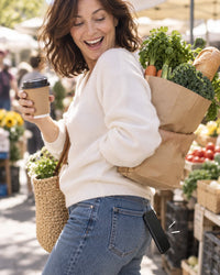 Woman at a market with full hands, her phone sliding out of her back jeans pocket