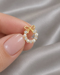 One bow wreath stud held on a fingertip, showing how small it is