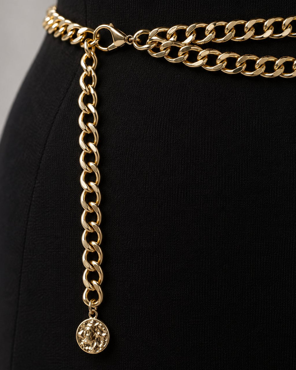 Close-up of the polished gold-tone curb links and the small coin charm at the end
