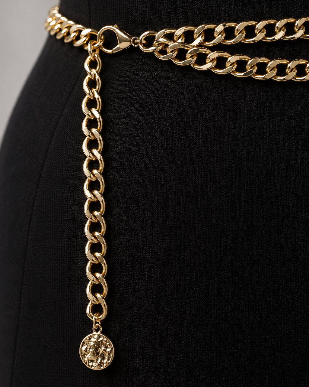 Close-up of the polished gold-tone curb links and the small coin charm at the end