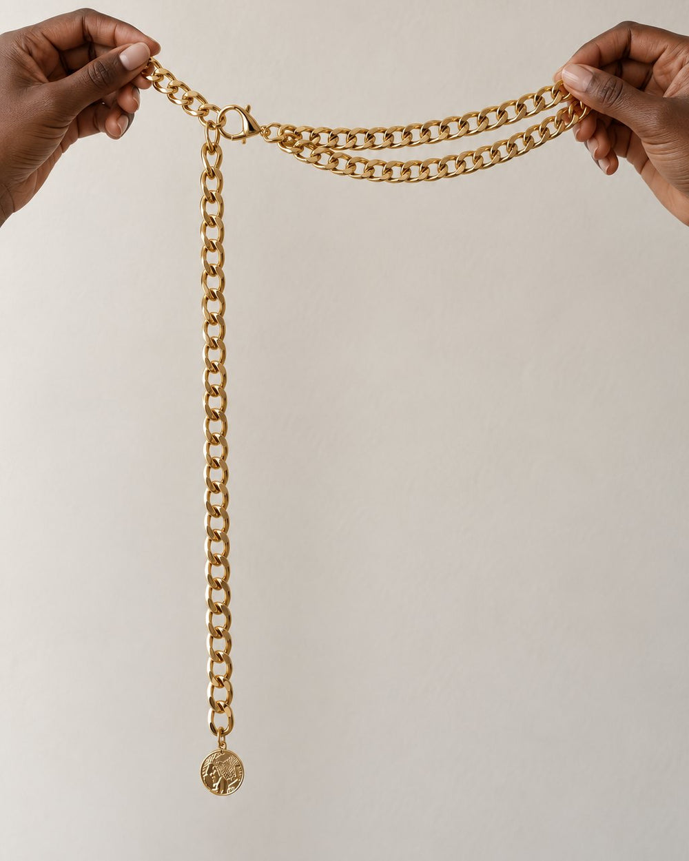 The gold double chain belt held up in two hands, showing both rows and the drop