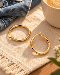 Gold-tone hoops on a linen dresser runner beside a denim jacket and a cup of coffee