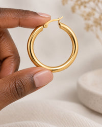 One chunky hoop held between finger and thumb to show its 1.5 in size