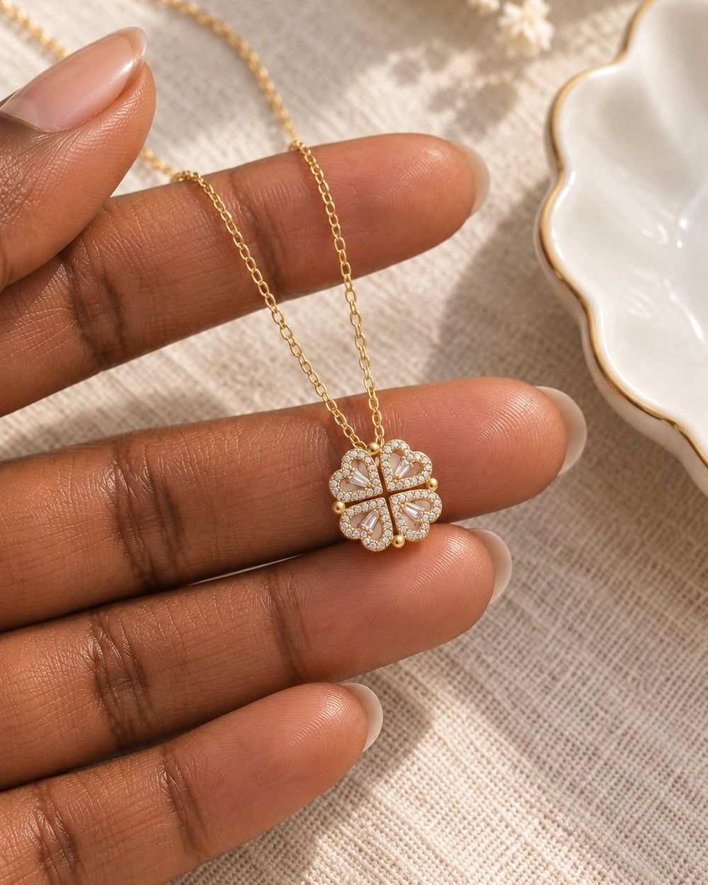 The clover pendant resting on a fingertip beside a ring dish, showing its dainty size