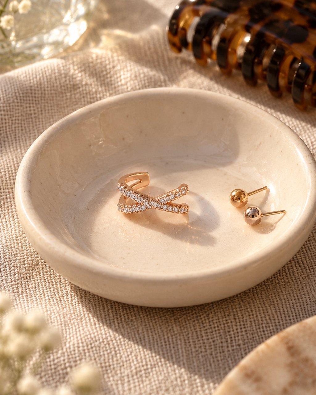 The ear cuff in a small ceramic dish beside stud earrings and a hair clip on a linen cloth