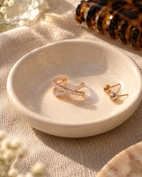 The ear cuff in a small ceramic dish beside stud earrings and a hair clip on a linen cloth