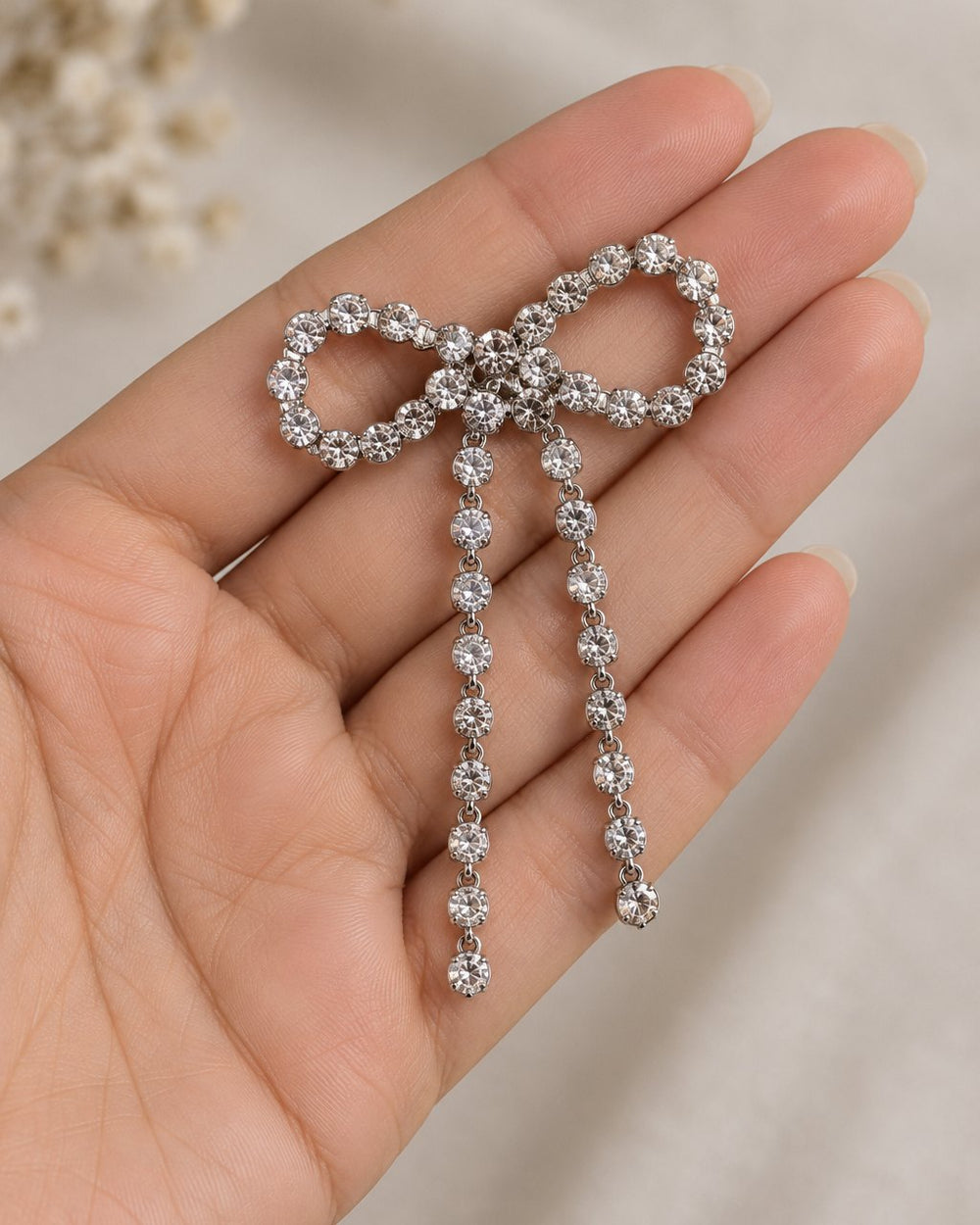 One sparkle bow earring lying across an open palm, its tails reaching past the fingers