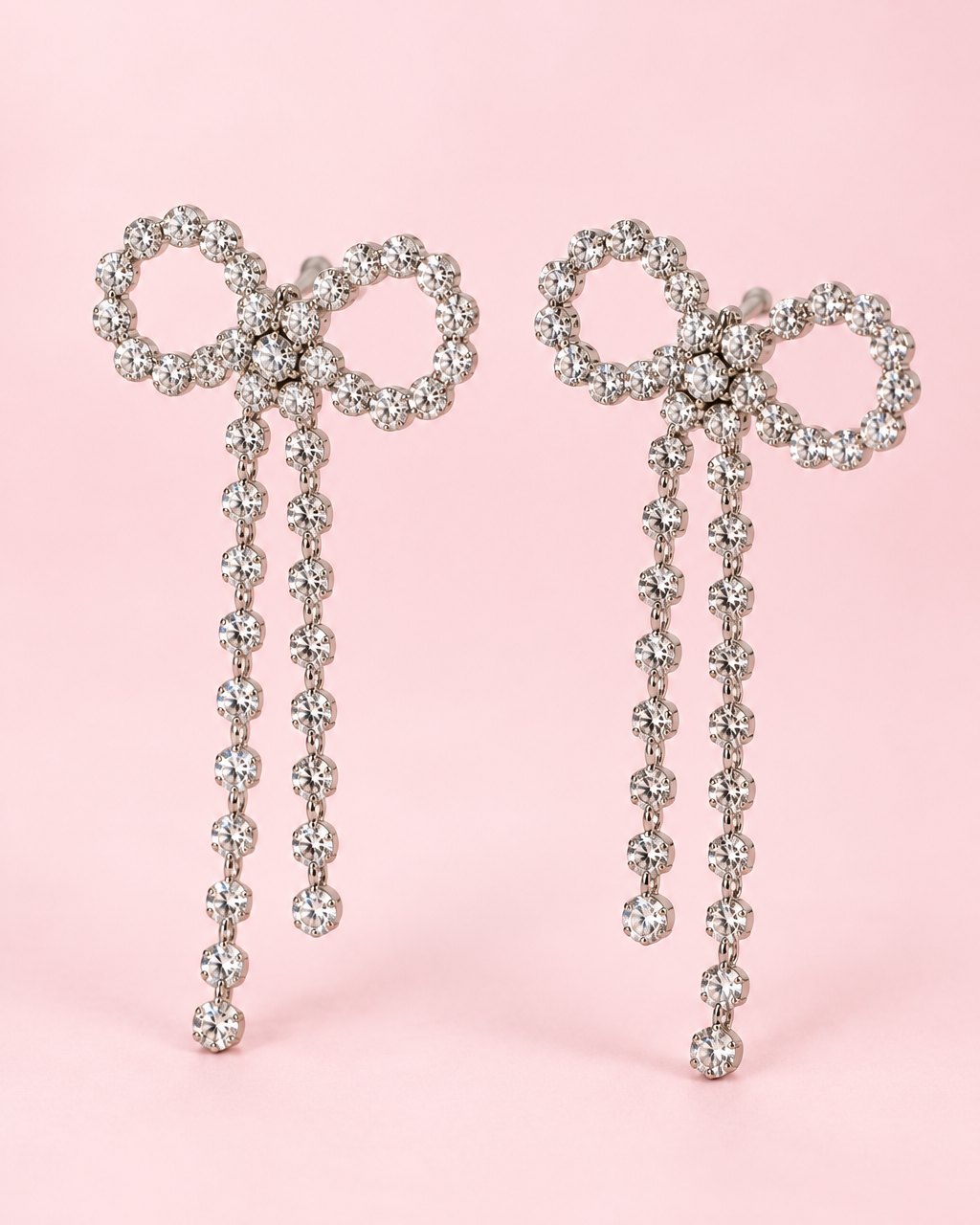 Pair of oversized silver-tone bow earrings outlined in clear stones, each with two long stone tails