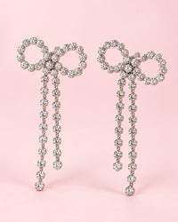 Pair of oversized silver-tone bow earrings outlined in clear stones, each with two long stone tails