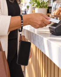 Woman paying at a café counter, her phone hanging from her wrist on the black crystal bead strap