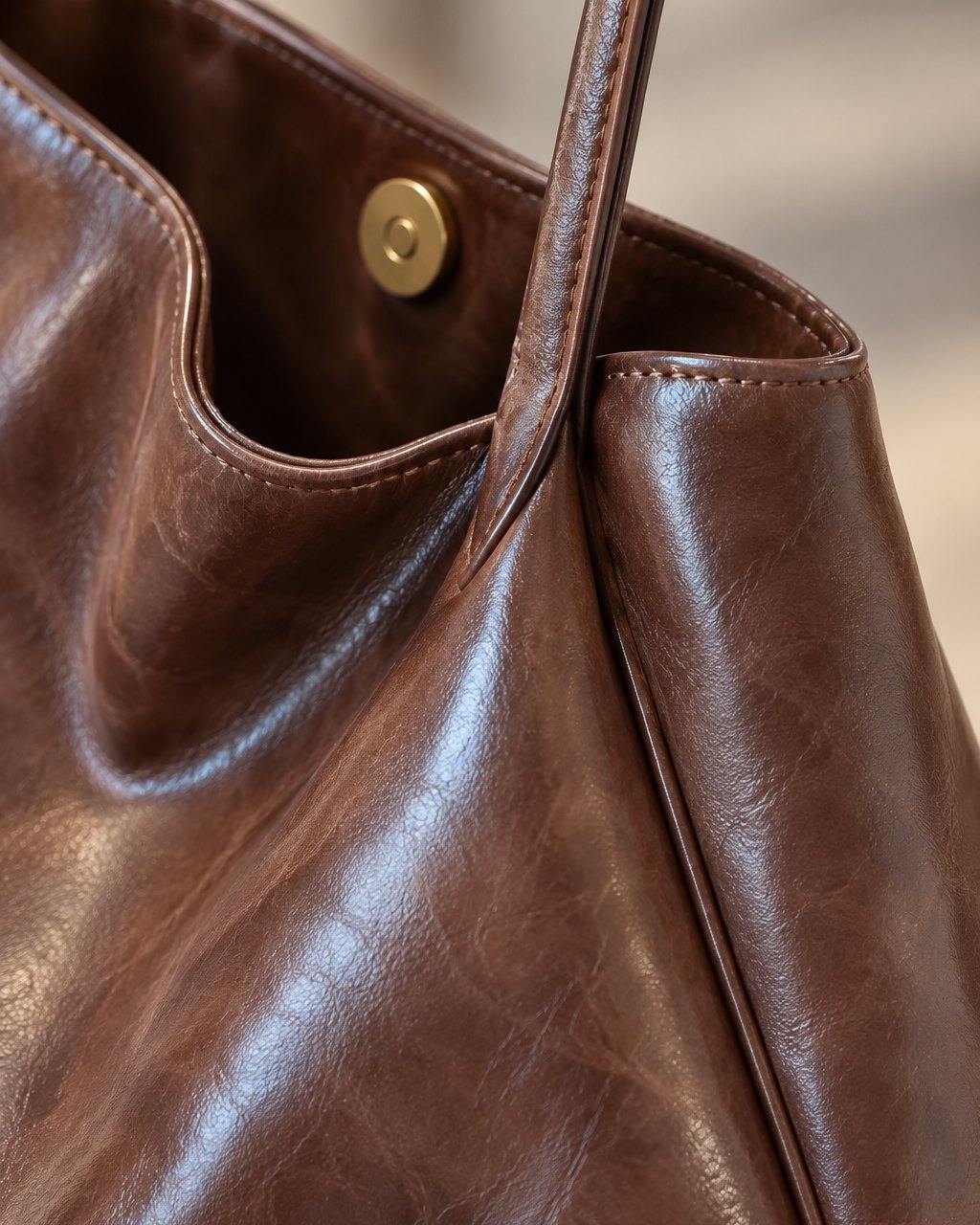 Close-up of the tote's glossy brown finish, a strap join and the magnetic snap at the top