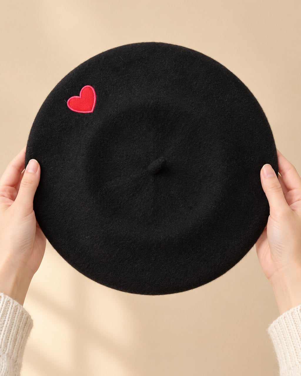 The black heart beret held flat in two hands, about the width of a dinner plate