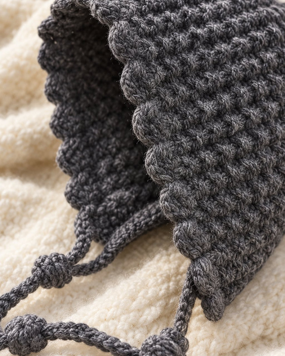 Close-up of the chunky grey knit stitch, wavy edge and small knots on the ties
