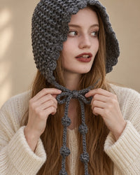 A woman ties the grey knit bonnet's long ties into a bow under her chin