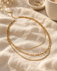 The layered necklace on cream linen beside a ceramic dish and a cup of coffee