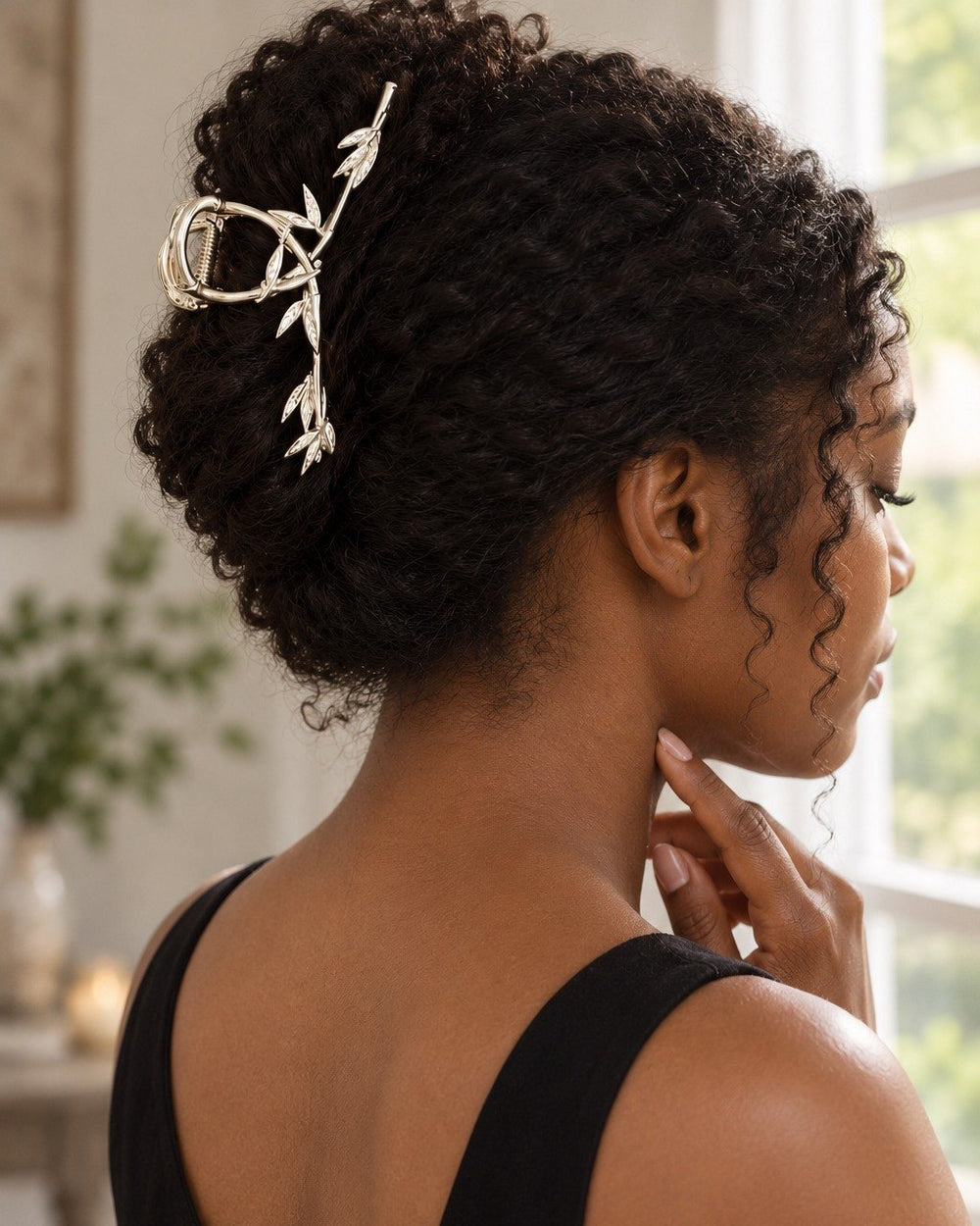 Woman in a black top at a window with her hair in a twisted bun held by the leaf clip