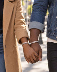 A couple walks down a sunny street hand in hand, each wearing one silver-tone curb bracelet