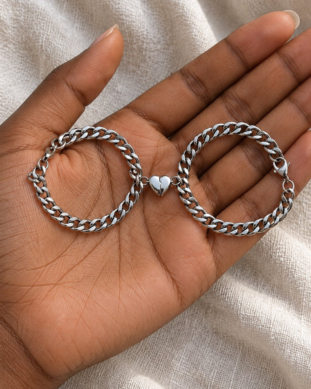 Both bracelets in one open palm, showing the curb links and the joined heart