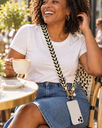 Woman laughing on a café terrace with the leaf-woven strap worn crossbody and her phone at her hip