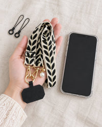 The woven strap loosely coiled in an open hand beside a phone in a clear case