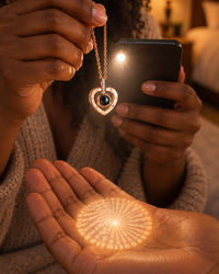 A phone torch shines through the heart pendant, casting a small glowing circle of tiny writing onto an open palm