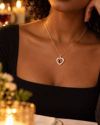 Woman in a black top wearing the rose gold-tone heart pendant below her collarbone at a candlelit dinner