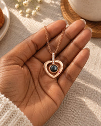 The heart pendant resting on an open palm next to a coffee cup, showing its small size