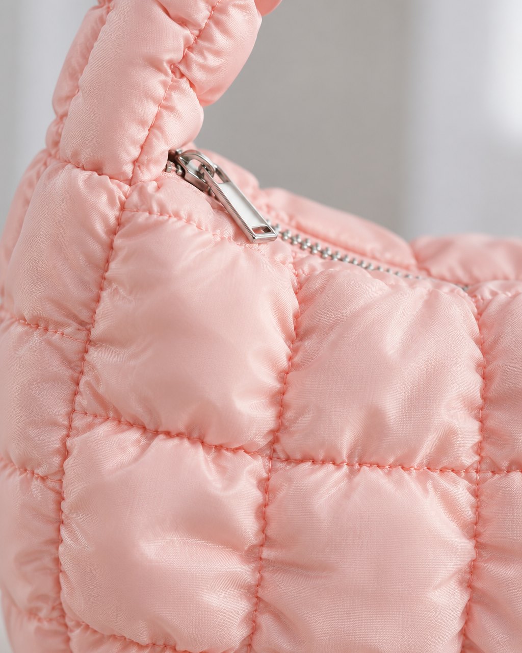 Close-up of the bag's puffy quilted squares and the small zip pull at the top