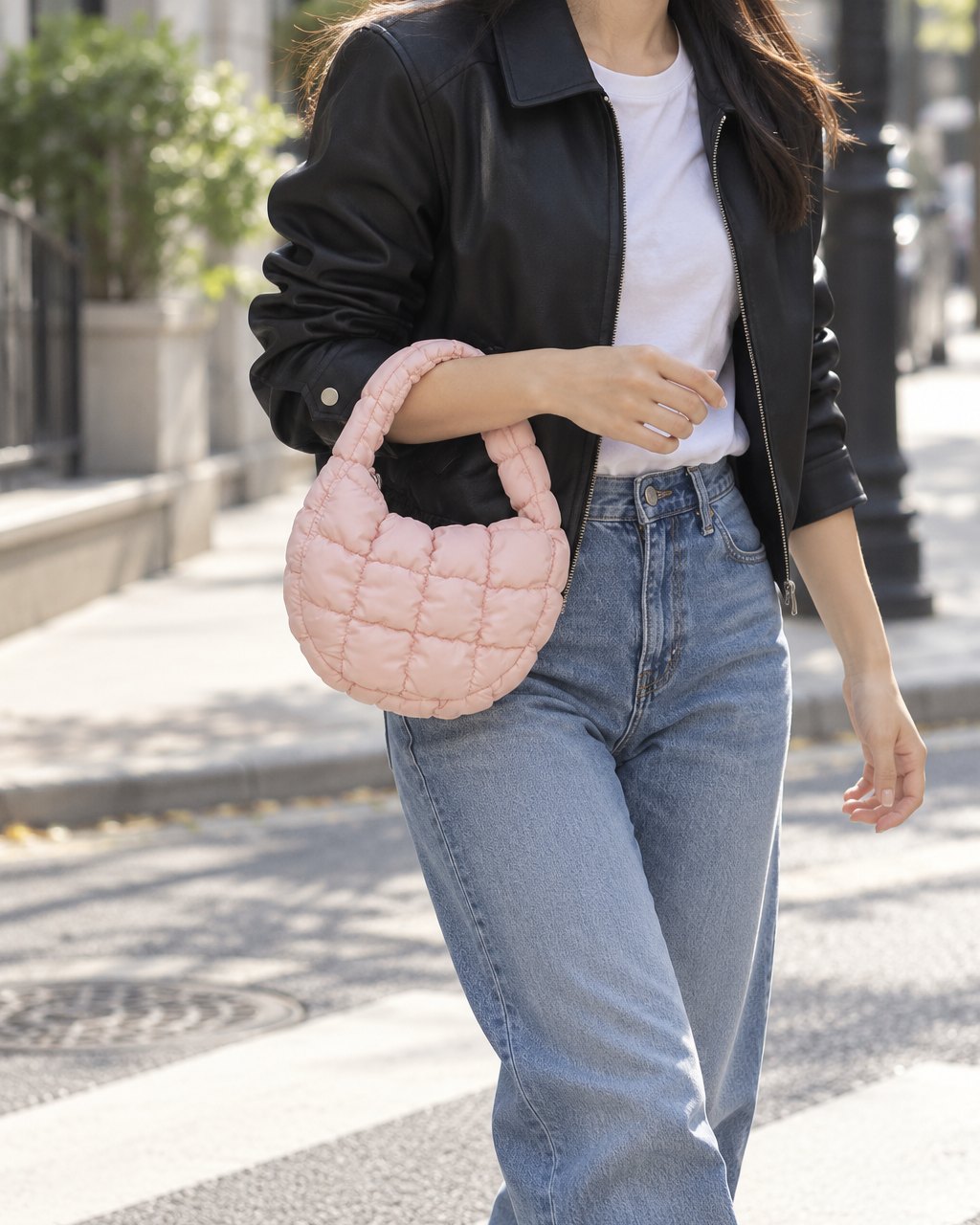 Woman in jeans and a white tee walking down a sunny street with the pink quilted bag on her wrist