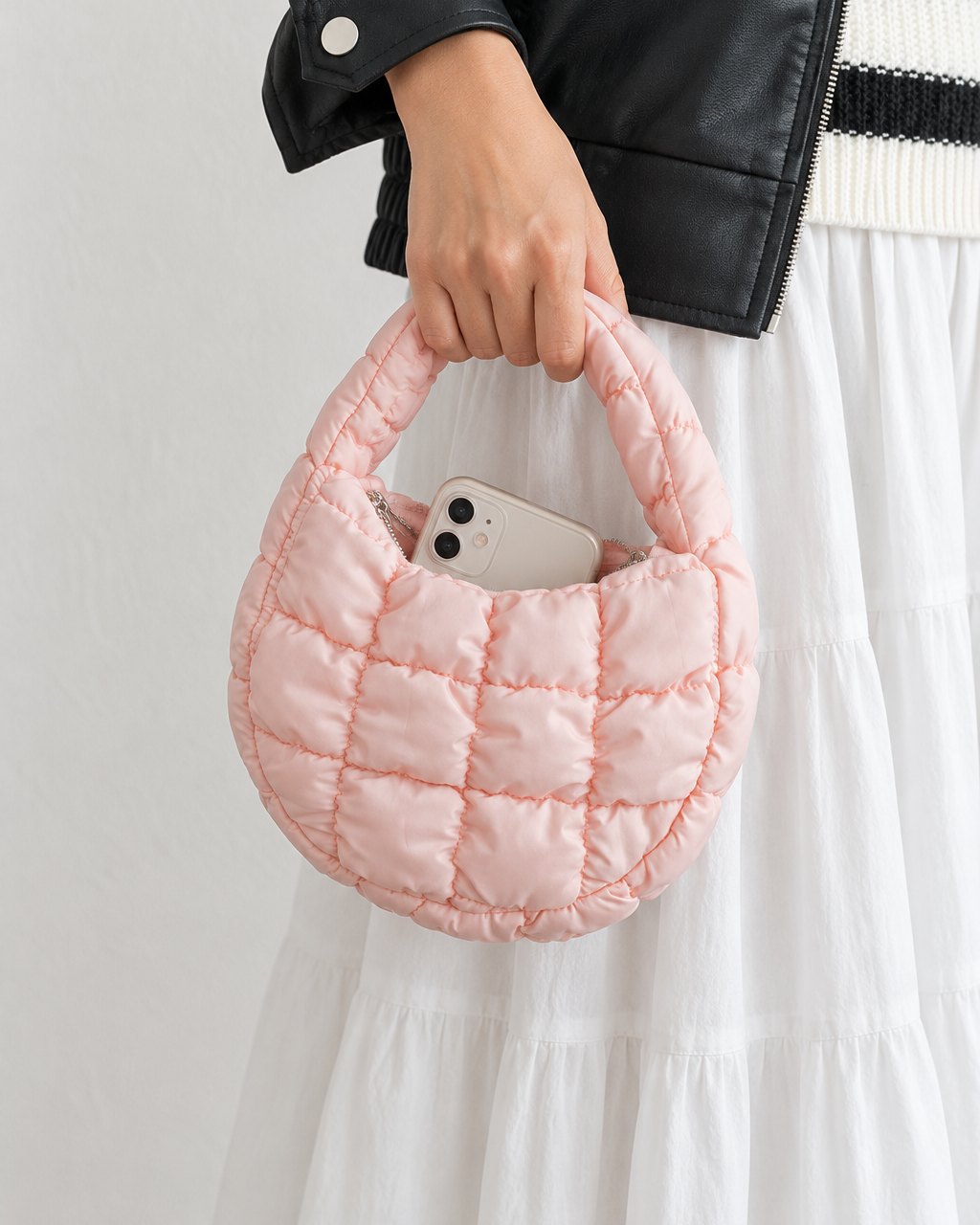A hand holds the mini bag by its top handle, a phone peeking out of the open zip