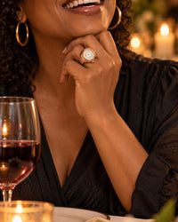 Woman at a candlelit dinner table resting her chin on her hand, the ring watch on her finger