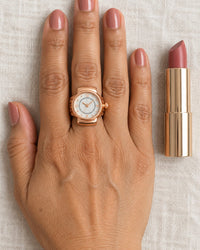 The ring watch on a woman's middle finger, with a lipstick beside her hand for size