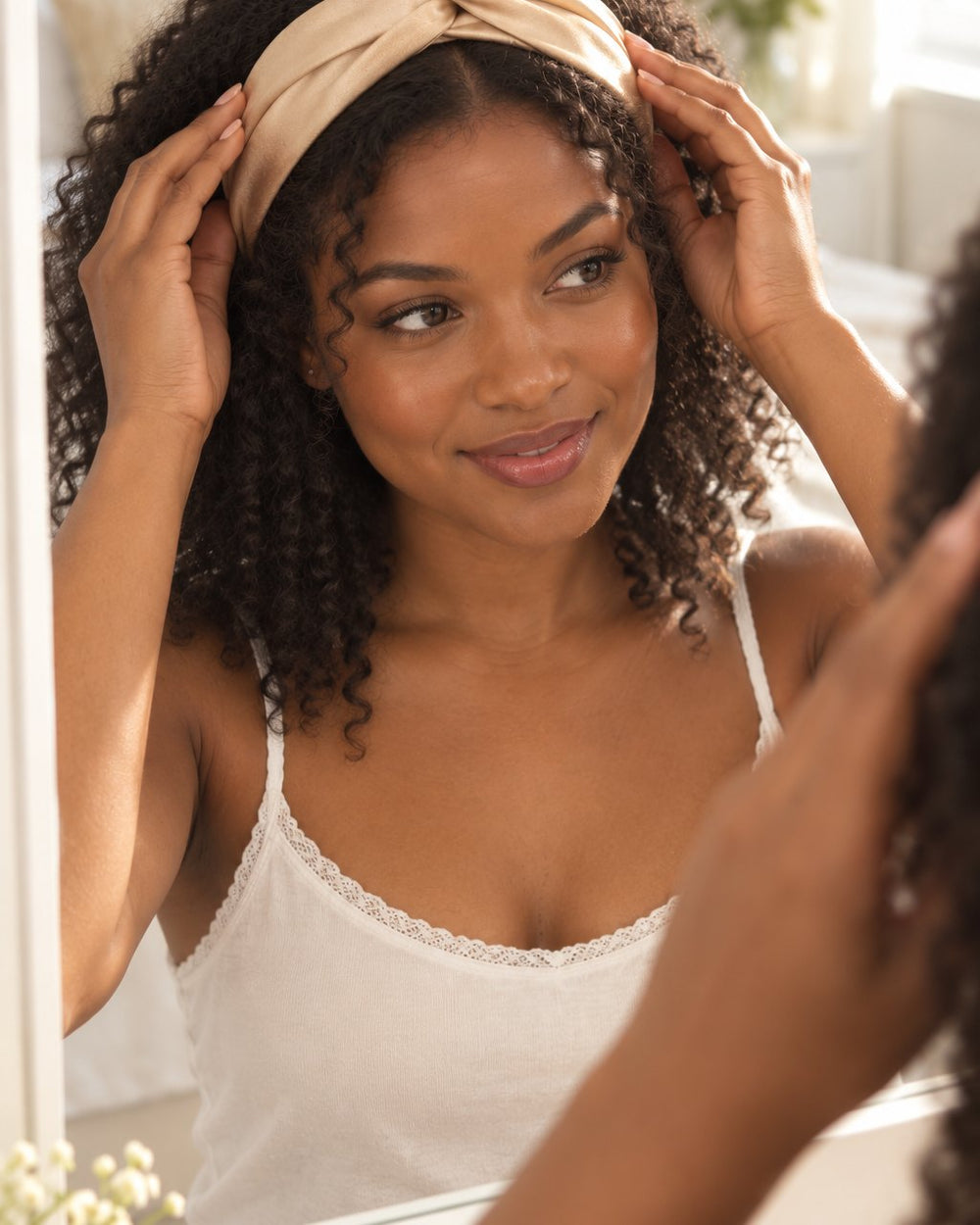 A woman pushes the champagne twist headband onto her loose wavy hair at a mirror