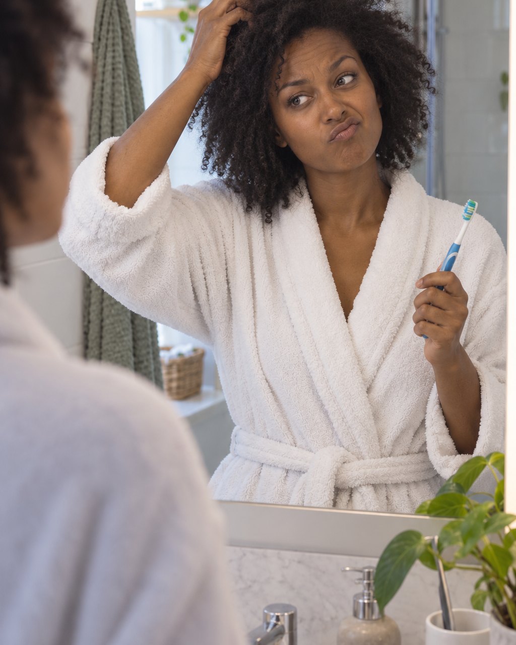 Woman pulling a face at flat, messy second-day hair in a bathroom mirror