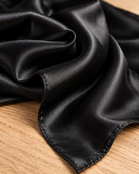 Close-up of the smooth, glossy weave and folded edge of the black satin scarf