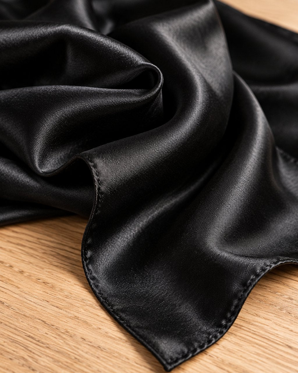 Close-up of the smooth, glossy weave and folded edge of the black satin scarf