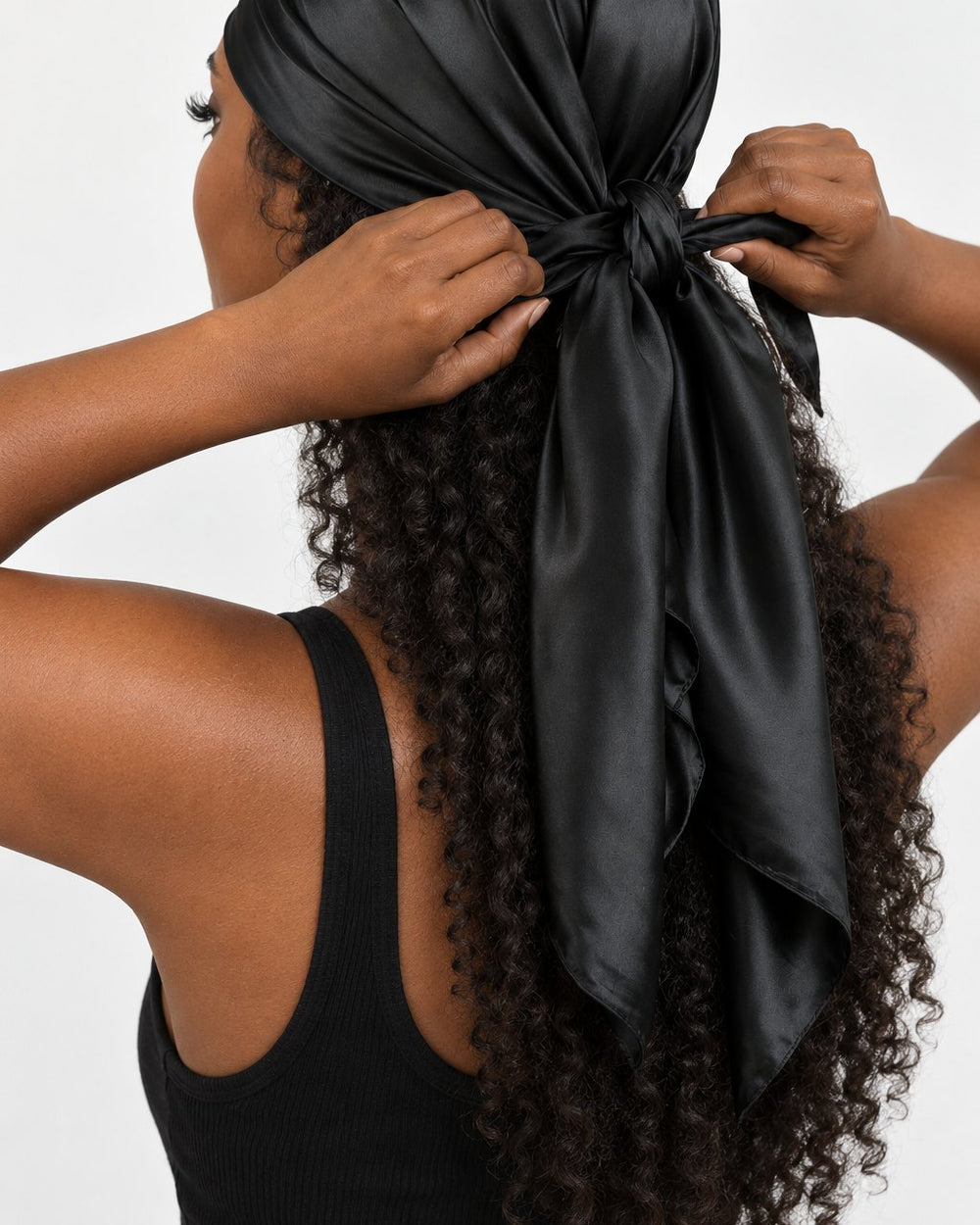 A woman ties the black satin scarf over her long hair at the nape of her neck