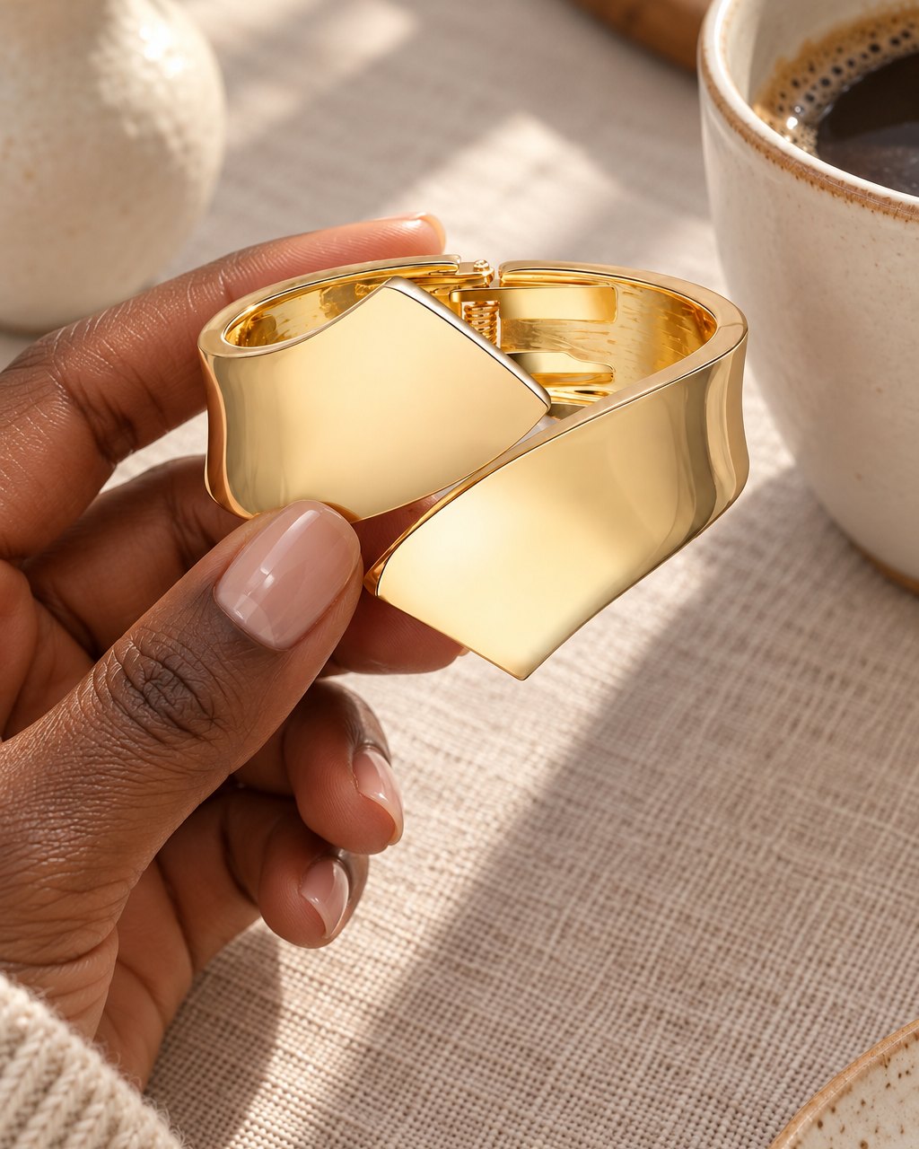 The cuff held in a hand beside a coffee cup, showing its wide band and bold size